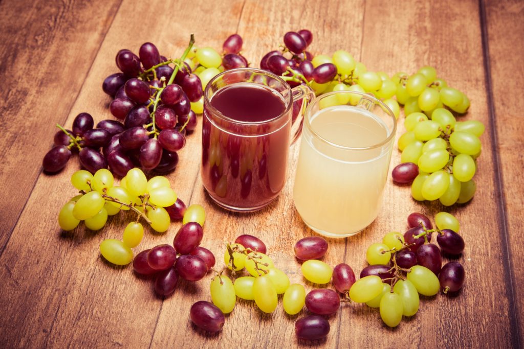 Glass of red stum and 2 glasses of white stum together with some green and red grapes photpgraphed on a piece of wood in retro style.