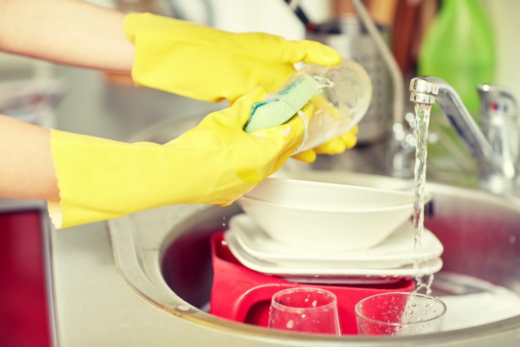 people, housework, washing-up and housekeeping concept - close up of woman hands in protective gloves washing dishes with sponge at home kitchen