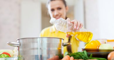 Woman in yellow pours oil from bottle into the pan. Focus on bottle