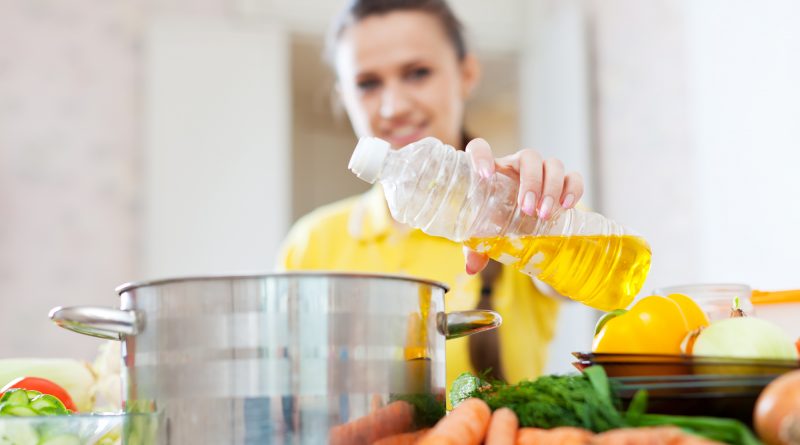 Woman in yellow pours oil from bottle into the pan. Focus on bottle