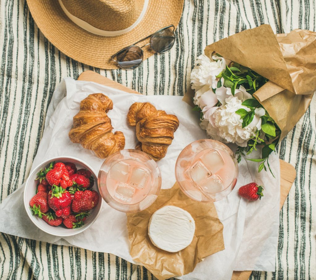 Flat-lay of rose wine, strawberries, croissants, brie cheese, flowers